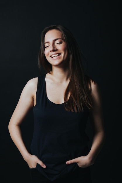 Foto de estúdio de uma jovem linda de blusa preta sorrindo e posando isolada em fundo preto