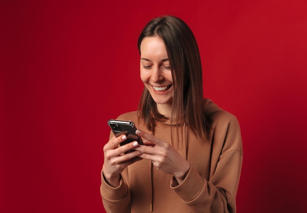 Foto de estúdio de uma jovem sorridente segurando e digitando uma mensagem em seu telefone