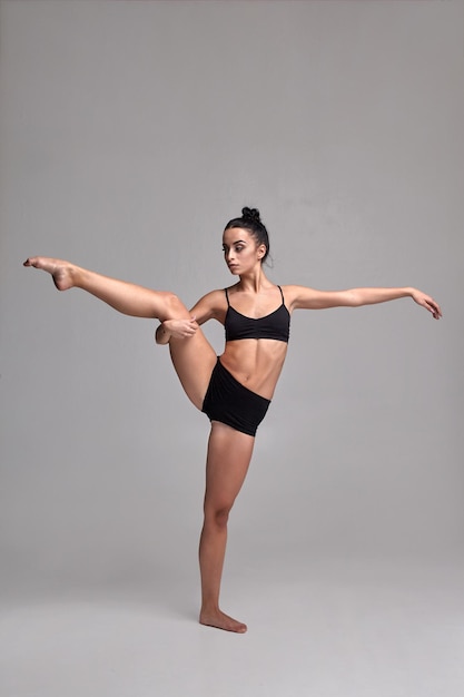 Foto de estúdio de uma linda bailarina vestida com maiô preto de duas peças fazendo um elemento de dança em um fundo cinza.