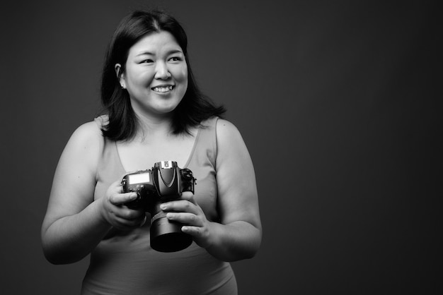 Foto de estúdio de uma linda mulher asiática com excesso de peso usando um vestido sem mangas contra um fundo cinza em preto e branco