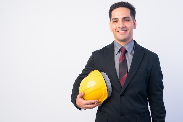 Foto de estúdio do bonito empresário persa de terno como engenheiro com capacete de segurança isolado contra branco