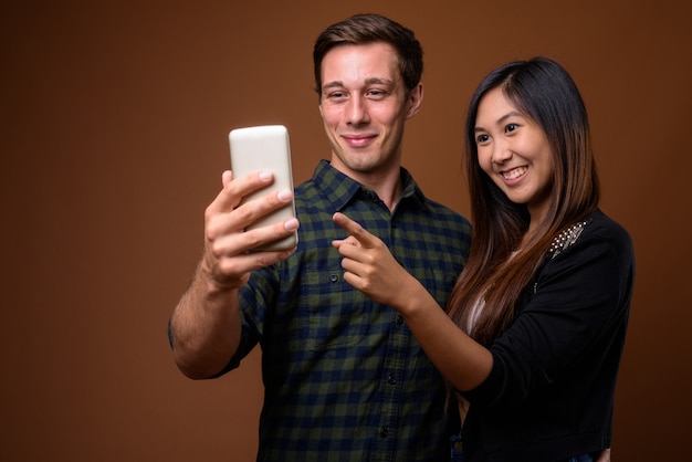 Foto de estúdio do jovem casal multiétnico na parede marrom