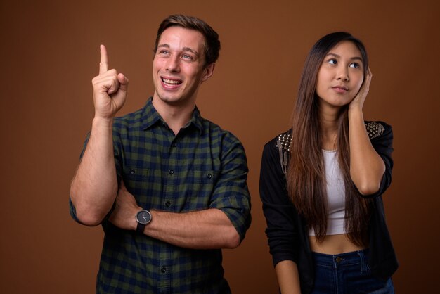 Foto de estúdio do jovem casal multiétnico na parede marrom