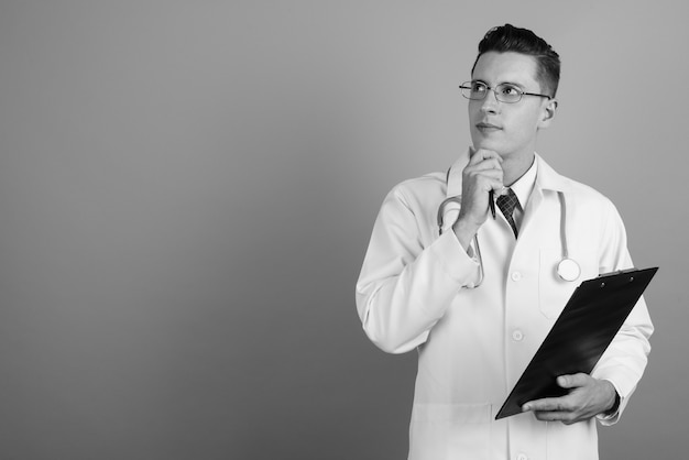 Foto de estúdio do médico jovem bonito usando óculos contra um fundo cinza em preto e branco