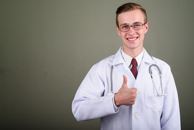 Foto de estúdio do médico jovem bonito usando óculos contra um fundo colorido