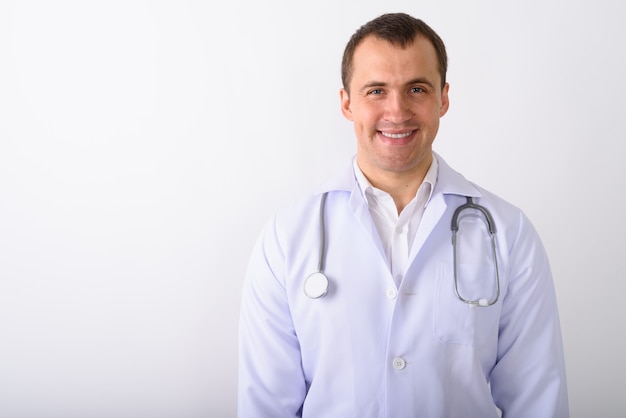 Foto de estúdio do médico jovem feliz e musculoso sorrindo contra w