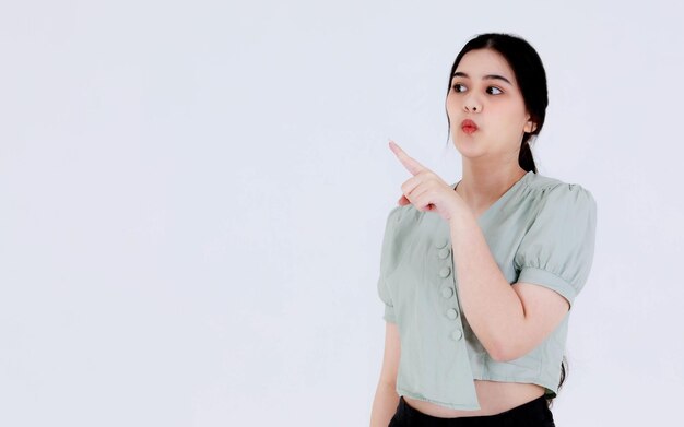 Foto de estúdio do modelo feminino adolescente engraçado jovem asiático com penteado de rabo de cavalo usando aparelho dentário para atendimento odontológico e top up de colheita de roupa casual segurando a mão apontando rindo sobre fundo branco.