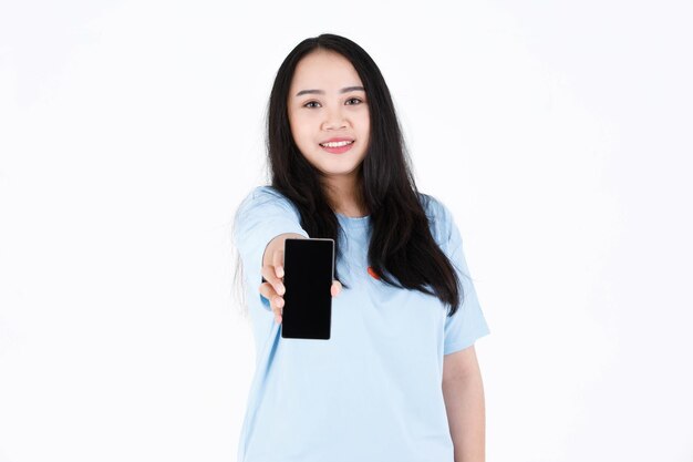 Foto de estúdio do modelo feminino de cabelo preto comprido gordo gordinho asiático em camiseta azul casual e sorrindo segurando o smartphone no fundo branco.