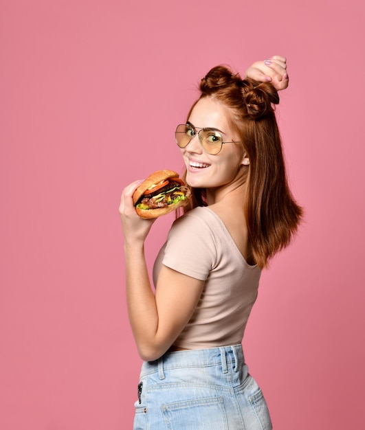 Foto de estúdio horizontal de uma bela jovem segurando um hambúrguer