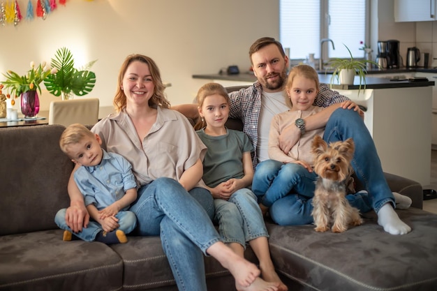 Foto de família retrato de família em que mãe pai filhas filho e cachorro estão sorrindo e abraçando no sofá em um ambiente aconchegante foco seletivo