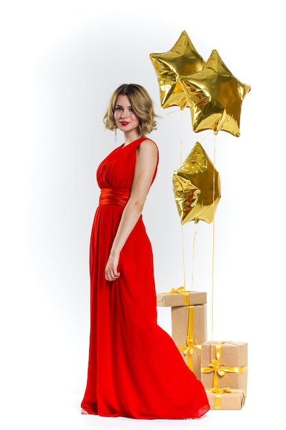 Foto de festa de senhora sexy elegância em um vestido vermelho com lábios vermelhos e cabelo loiro lindo encaracolado, sorrindo. Fundo de balões de ar de ouro e presentes. Conceito de venda