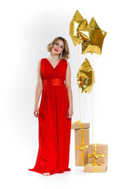 Foto de festa de senhora sexy elegância em um vestido vermelho com lábios vermelhos e cabelo loiro lindo encaracolado, sorrindo. Fundo de balões de ar de ouro e presentes. Conceito de venda