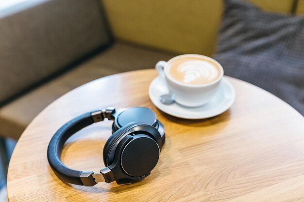 Foto de fones de ouvido sem fio pretos e xícara de café branca na mesa de madeira