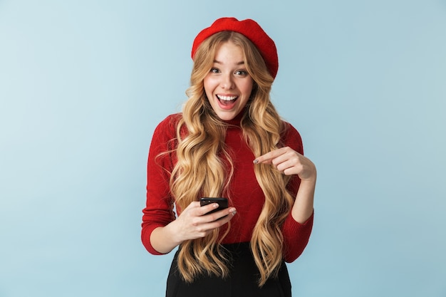 Foto de garota atraente de 20 anos usando boina vermelha usando smartphone isolada