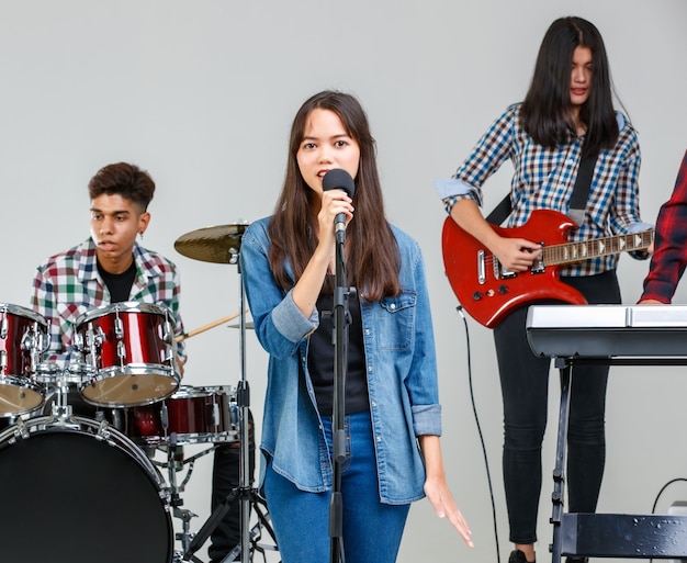 Foto de grupo de amigos adolescentes tocando a música e cantando juntos. Alunos juniores tocam guitarra elétrica, bateria e teclado. Uma jovem cantora cantando uma música com um músico ao fundo