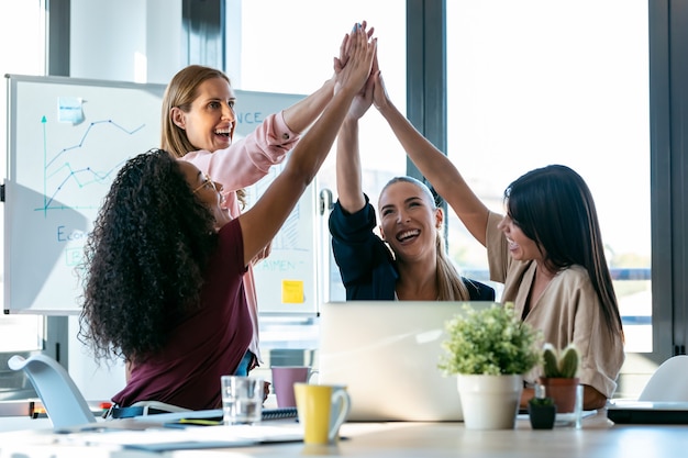 Foto de grupo de mulheres de negócios inteligentes bem-sucedidos, segurando a mão direita no lugar de coworking.