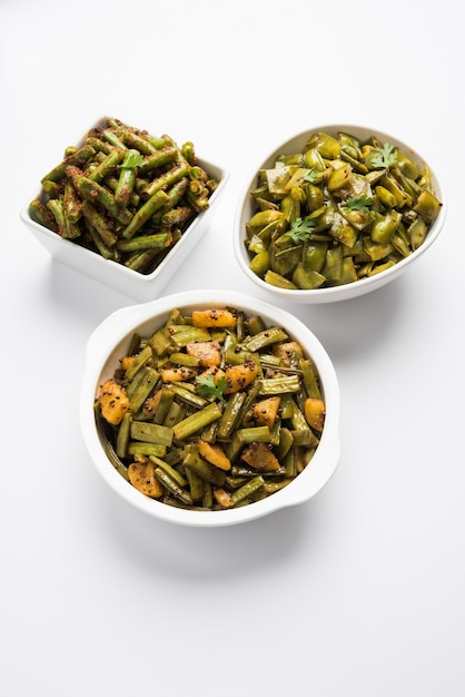 Foto de grupo de receita de vegetais de estilo indiano, como feijão verde, feijão gowar ou cluster e bhindi ou dedo feminino OU quiabo. Servido em tigela de cerâmica branca sobre fundo branco. Foco seletivo