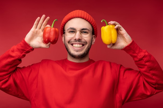 Foto de homem atraente com barba de óculos e roupas vermelhas. macho tem papéis nas mãos, mostra amor a vegetais isolados sobre fundo vermelho.