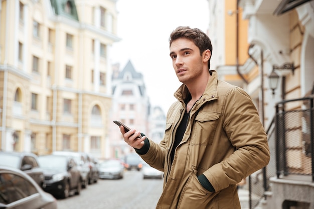 Foto de homem bonito, andando na rua e conversando ao lado de seu telefone ao ar livre. Olhe para o lado.