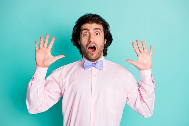 Foto de homem chocado e assustado de cabelo encaracolado vestido de camisa rosa com dois braços isolado fundo de cor turquesa