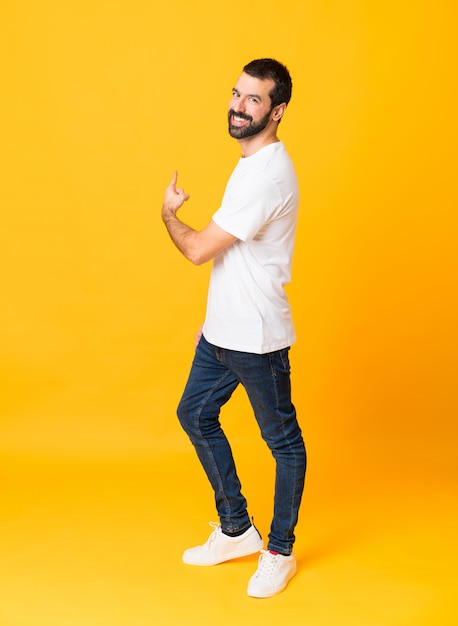 Foto de homem com barba sobre amarelo isolado apontando para trás