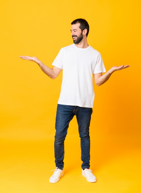 Foto de homem com barba sobre amarelo isolado segurando copyspace com as duas mãos