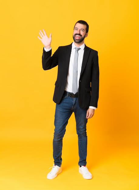 Foto de homem de negócios sobre amarelo isolado saudando com mão com expressão feliz