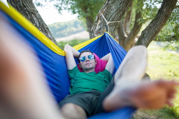 Foto de homem de óculos de sol deitado na rede na floresta