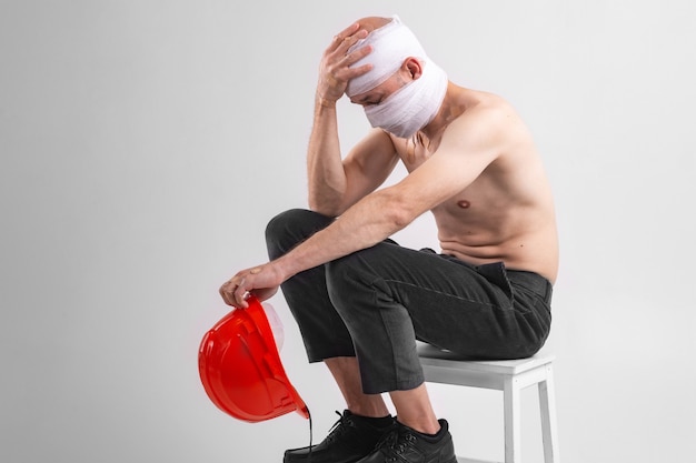 Foto de homem desesperado com a cabeça enfaixada, senta-se em uma cadeira com capacete protetor