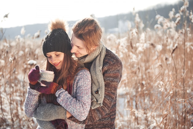 Foto de homem feliz e mulher bonita com copos ao ar livre no inverno. Férias de inverno e férias. Casal de Natal de homem e mulher feliz bebem vinho quente. Casal apaixonado