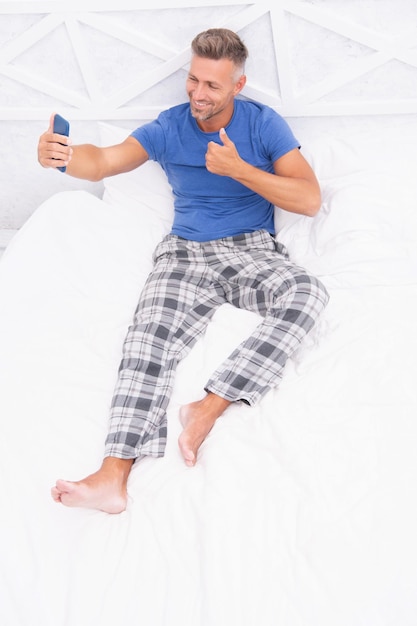 Foto de homem feliz por videochamada com telefone em casa Homem por videochamada com telefone no quarto