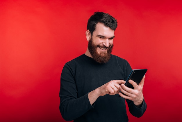 Foto de homem feliz surfando na internet com o tablet em pé sobre o espaço vermelho