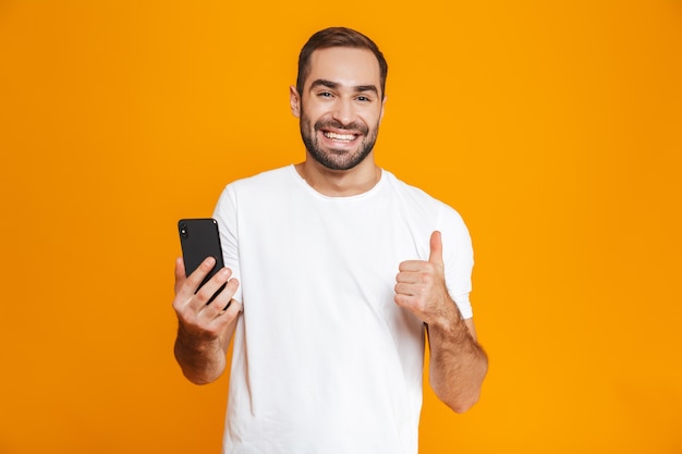 Foto de homem positivo de 30 anos em roupa casual sorrindo e segurando um smartphone, isolada