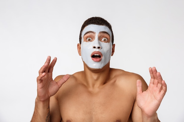 Foto de homem sem camisa, sorrindo e aplicando creme para o rosto isolado sobre o branco