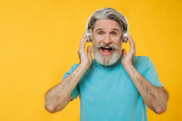 Foto foto de homem sênior grisalho em fones de ouvido cantando isolado em fundo amarelo