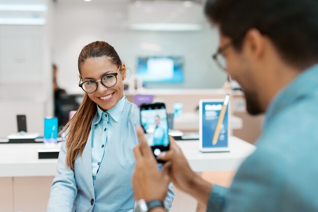 Foto de homem tomada de sua esposa em pé na loja de tecnologia. foco seletivo na mulher.