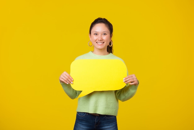 Foto de jovem alegre está segurando uma bolha de texto no espaço amarelo, sorrindo para a câmera.