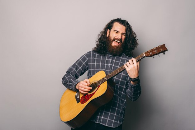 Foto de jovem com cabelo comprido e barba pagando no violão
