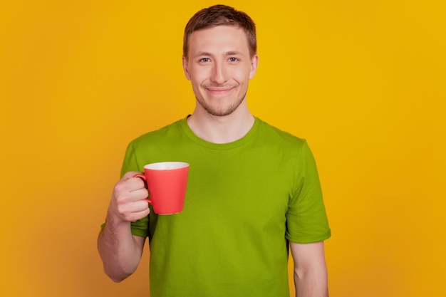 Foto de jovem com sorriso positivo e feliz, beber uma xícara de café quente isolada sobre o fundo de cor amarela