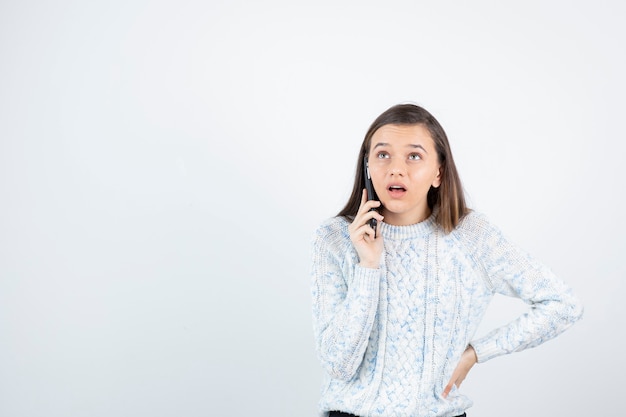 Foto de jovem com suéter falando com alguém pelo celular.