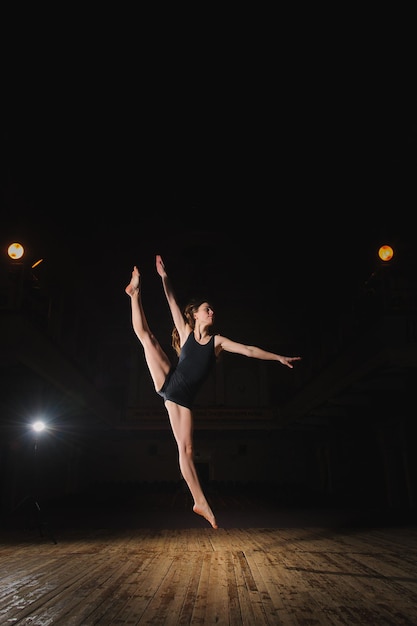 Foto de jovem dançarina morena fazendo salto dividido no palco no teatro com destaque dançarina descalça