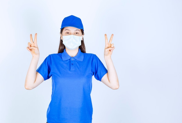 Foto de jovem de uniforme usando máscara médica e mostrando sinal de vitória.