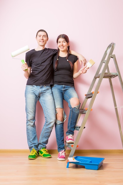 Foto de jovem e homem com rolo de pintura em pé perto da escada