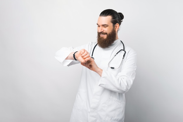 Foto de jovem médico em pé sobre uma parede branca e usando smartwatch