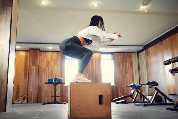Foto de jovem mulher malhando com uma caixa no ginásio. caixa de atleta feminina pulando em um ginásio de treinamento funcional