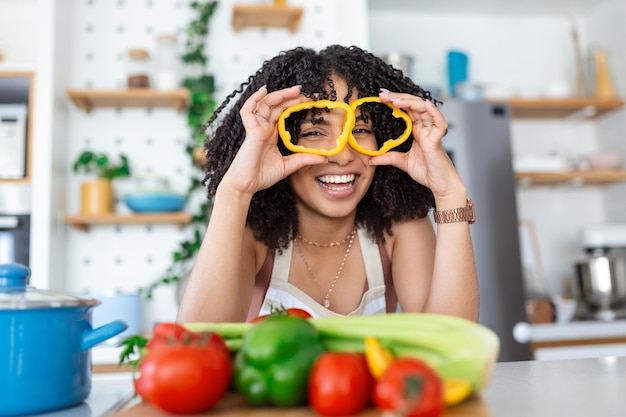 Foto de jovem sorrindo enquanto cozinha salada com legumes frescos no interior da cozinha em casa