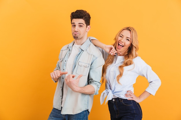 Foto de jovens modernos sorrindo e se divertindo enquanto um homem aponta o dedo para uma mulher, isolada na parede amarela