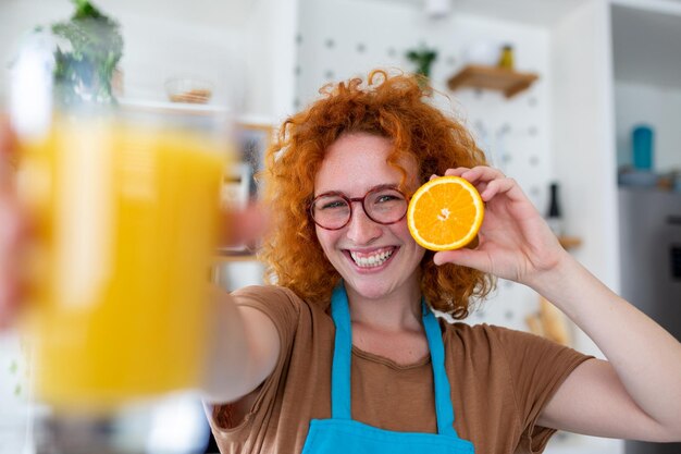 Foto de linda mulher caucasiana sorrindo e segurando duas partes de laranja enquanto cozinha salada de legumes no interior da cozinha em casa