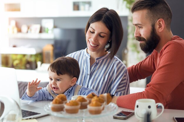 Foto foto de lindos pais jovens com eles bebê procurando desenhos animados no laptop em casa.