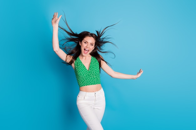 Foto de menina alegre positiva desfrutar, alegrar-se vento sopro corte de cabelo, levantar mão usar roupas de boa aparência isoladas sobre fundo de cor azul